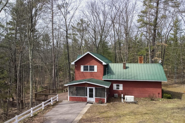 view of front of property with a sunroom, a wooded view, metal roof, a chimney, and fence