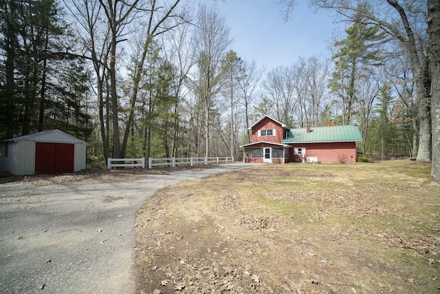 exterior space with an outdoor structure, driveway, a storage shed, metal roof, and fence