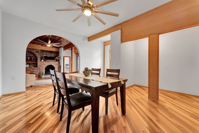 3628 Ford Ave, Jackson, MI 49203 - dining room featuring ceiling fan, arched walkways, light wood-type flooring, a fireplace, and brick wall
