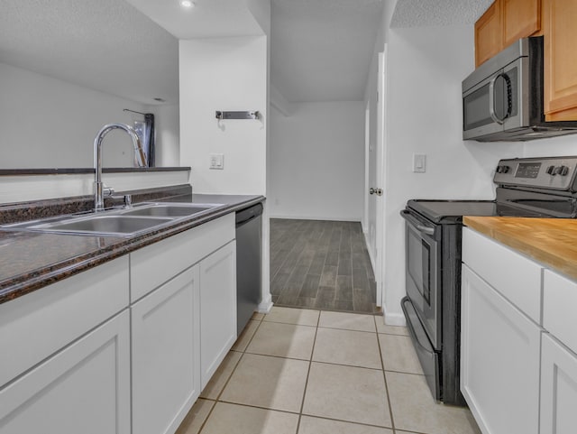 2401 Packard St Unit 31D, Ann Arbor, MI 48104 - kitchen with light tile patterned floors, a sink, stainless steel appliances, white cabinets, and a textured ceiling