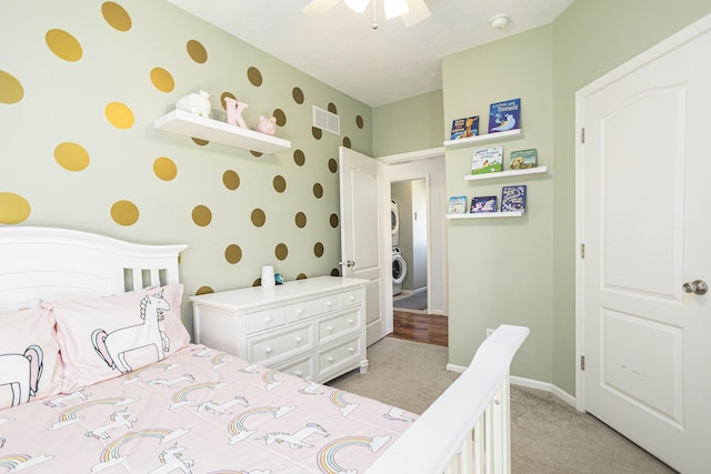 bedroom with a ceiling fan, visible vents, light carpet, stacked washer and clothes dryer, and baseboards