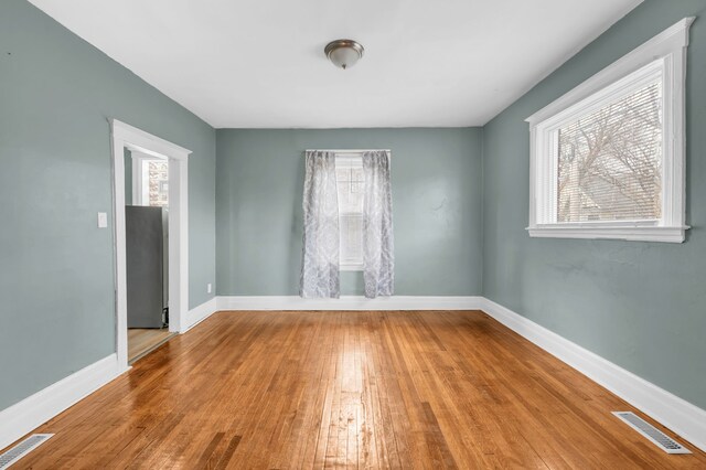 empty room featuring wood-type flooring, visible vents, and baseboards