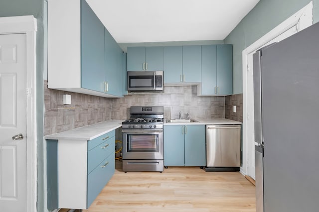 kitchen with blue cabinetry, appliances with stainless steel finishes, light countertops, light wood finished floors, and backsplash