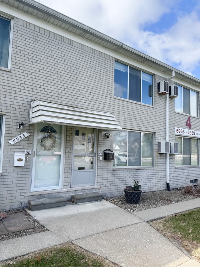 5959 Alan Dr Unit 57, Brighton, MI 48116 - view of exterior entry with a wall unit AC and brick siding