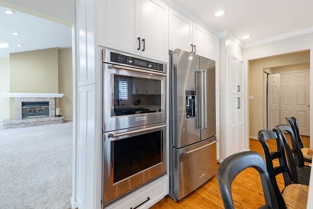 7837 Oak River Dr, Grosse Ile, MI 48138 - kitchen with ornamental molding, white cabinets, recessed lighting, appliances with stainless steel finishes, and a brick fireplace
