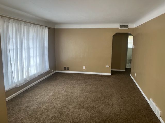 spare room featuring dark carpet, arched walkways, and visible vents
