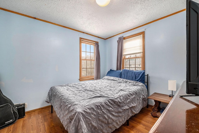 bedroom with a textured ceiling, wood finished floors, baseboards, and ornamental molding