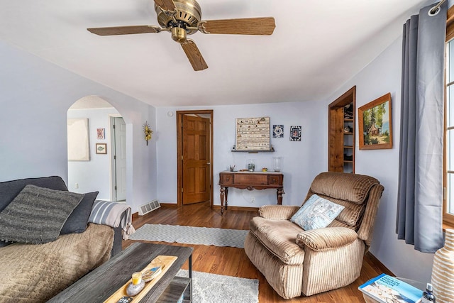 living room with arched walkways, wood finished floors, ceiling fan, and visible vents