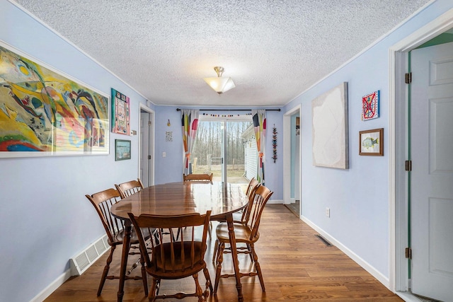 dining space featuring visible vents, baseboards, wood finished floors, and a textured ceiling