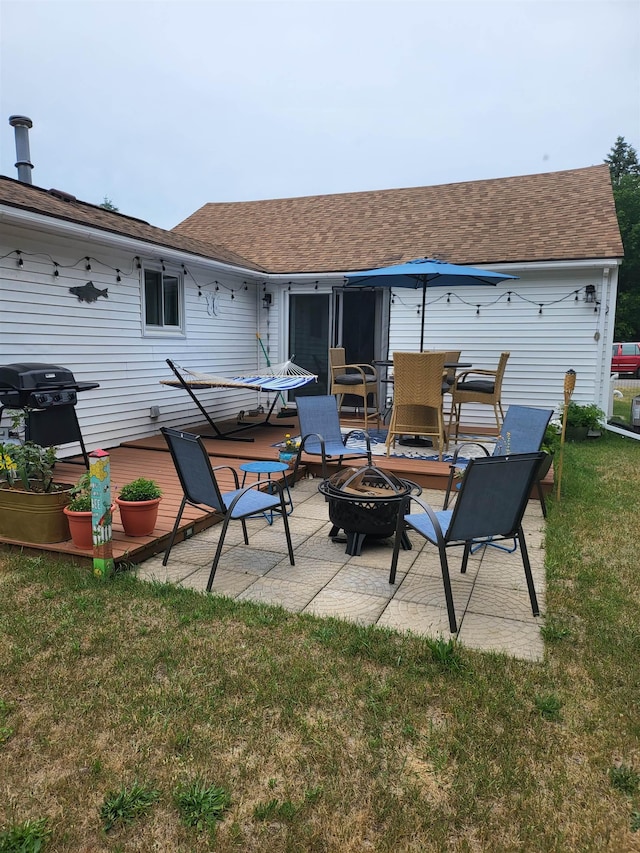 rear view of property featuring a patio, a shingled roof, a yard, and an outdoor fire pit