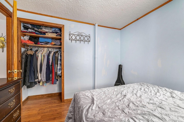 bedroom with a closet, baseboards, ornamental molding, a textured ceiling, and wood finished floors