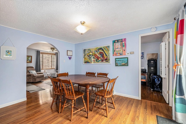 dining space featuring arched walkways, a textured ceiling, baseboards, and wood finished floors