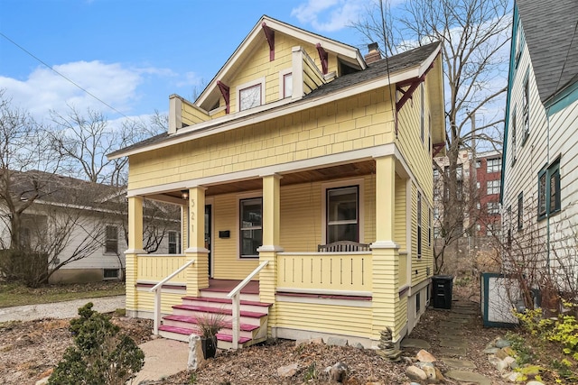 view of front of property featuring a chimney, a shingled roof, and covered porch