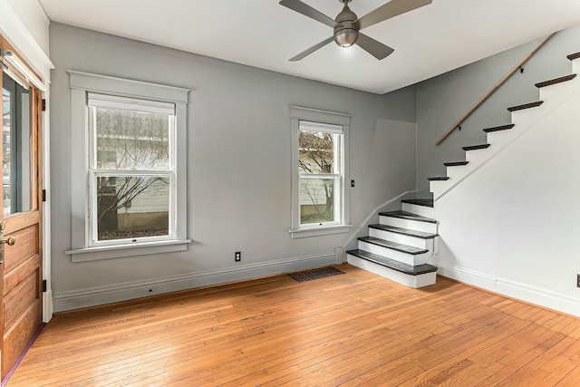 unfurnished living room featuring stairway, baseboards, a ceiling fan, and light wood finished floors