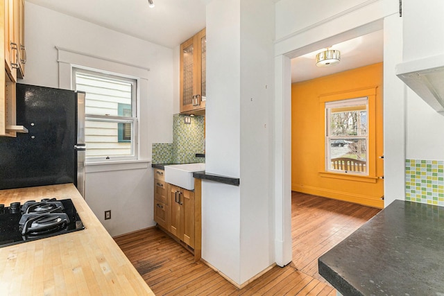 kitchen featuring light wood-style flooring, black gas stovetop, freestanding refrigerator, decorative backsplash, and a sink