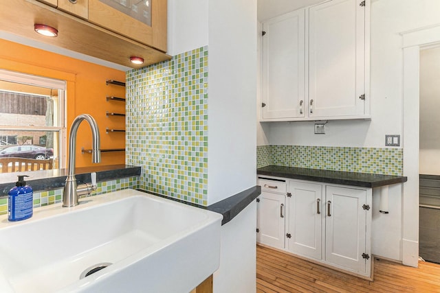 kitchen with light wood-type flooring, white cabinetry, dark countertops, decorative backsplash, and a sink
