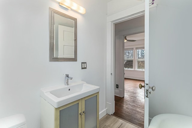 half bathroom featuring toilet, wood finished floors, vanity, and baseboards