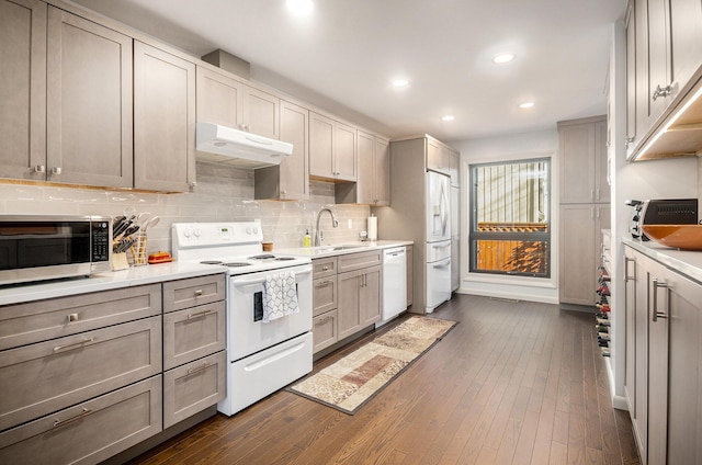 kitchen with white appliances, dark wood-type flooring, under cabinet range hood, a sink, and backsplash