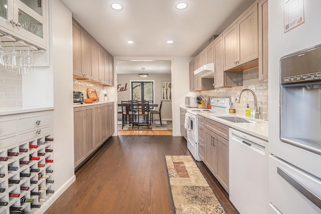 kitchen with white appliances, light countertops, under cabinet range hood, dark wood-type flooring, and a sink
