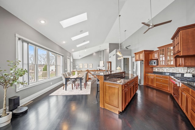 kitchen featuring a breakfast bar, glass insert cabinets, brown cabinetry, a skylight, and appliances with stainless steel finishes