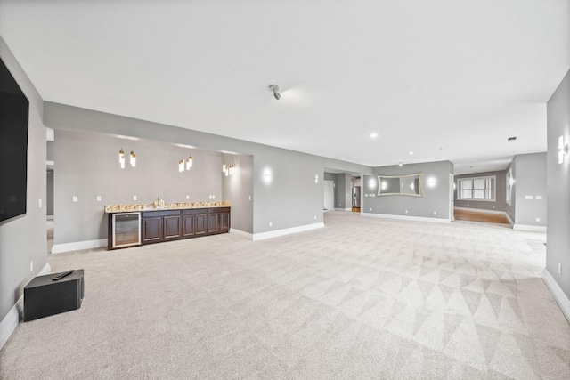 unfurnished living room featuring light carpet, wet bar, and baseboards