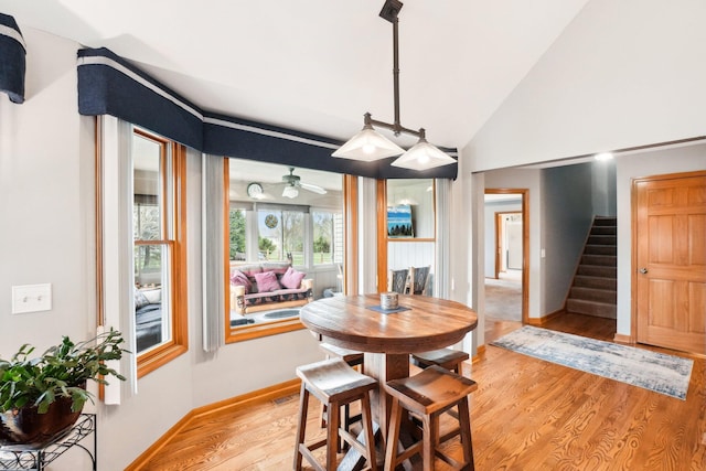 dining space with light wood-type flooring, baseboards, a ceiling fan, stairs, and lofted ceiling