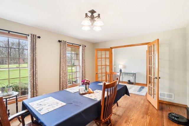 dining space featuring visible vents, baseboards, a chandelier, wood finished floors, and french doors