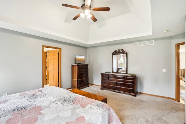 carpeted bedroom with visible vents, a tray ceiling, baseboards, and a ceiling fan