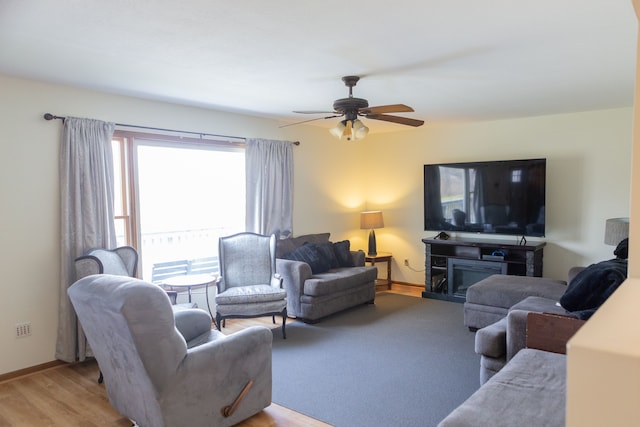 living room with light wood-style flooring, ceiling fan, a glass covered fireplace, and baseboards