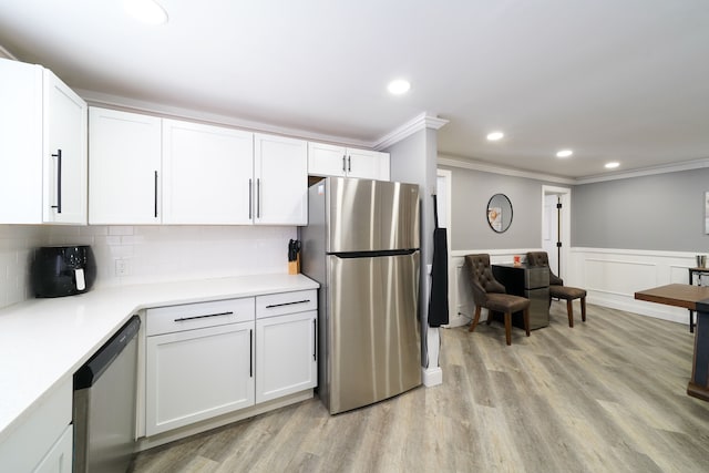 kitchen with light wood-style flooring, crown molding, a wainscoted wall, white cabinets, and stainless steel appliances