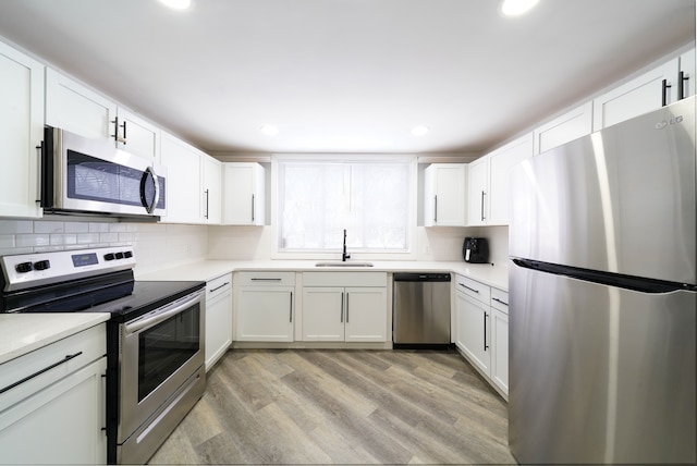 kitchen featuring a sink, light countertops, appliances with stainless steel finishes, white cabinetry, and light wood-style flooring
