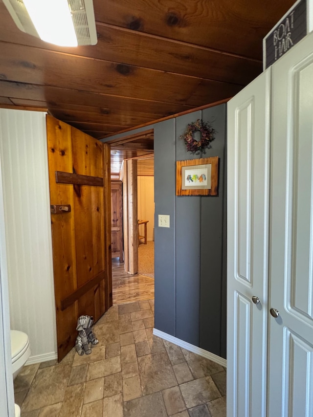 hallway featuring wood ceiling, stone tile flooring, wood walls, and baseboards