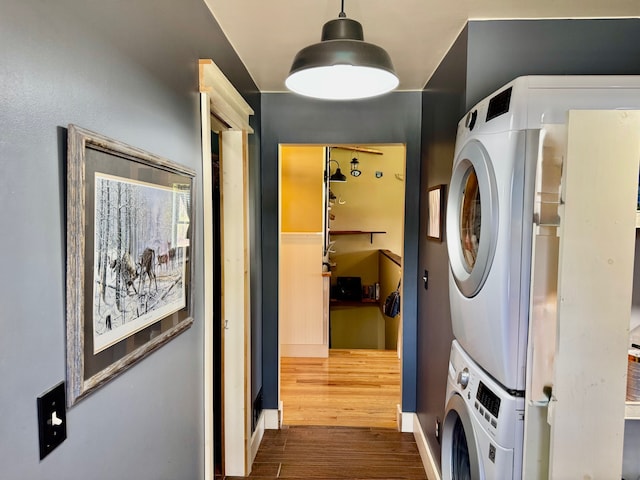 washroom featuring stacked washer / drying machine, laundry area, and dark wood-type flooring