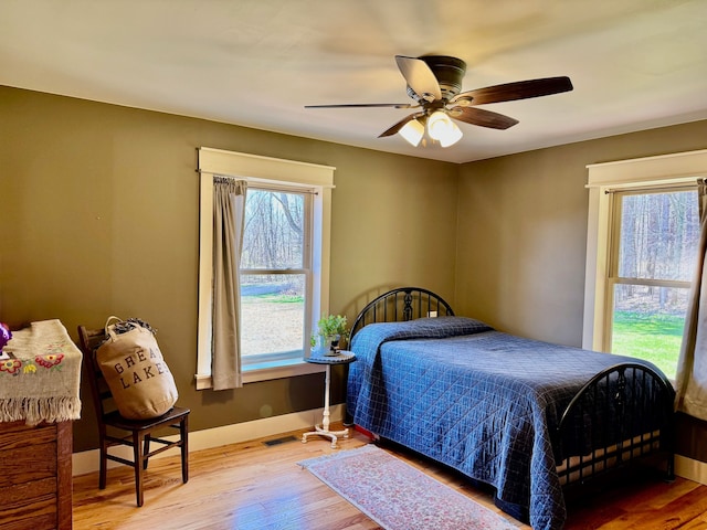 bedroom with ceiling fan, baseboards, multiple windows, and wood finished floors