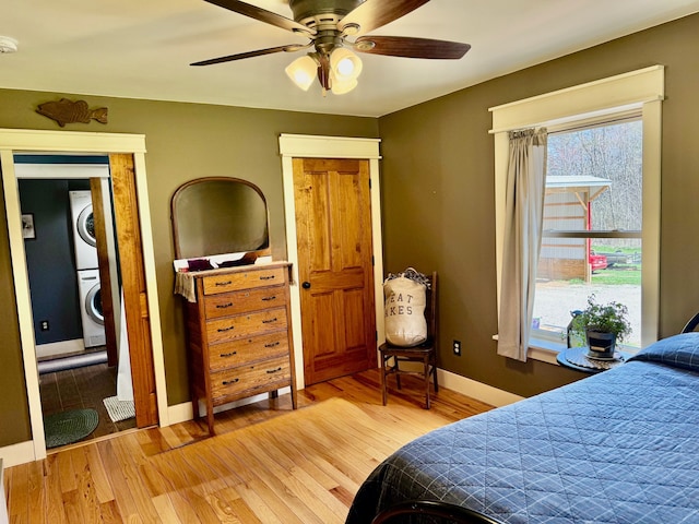 bedroom featuring baseboards, stacked washer and clothes dryer, light wood finished floors, and multiple windows