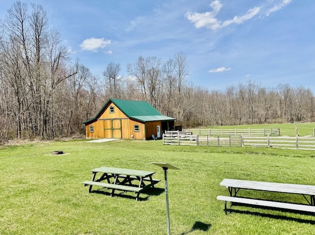 surrounding community with fence, a barn, a view of trees, an outbuilding, and a lawn