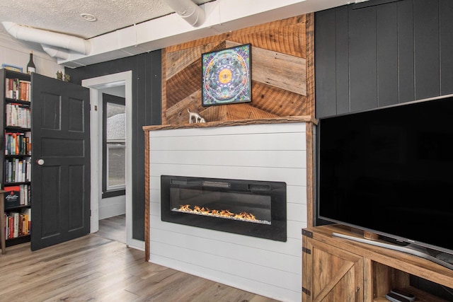 12934 Wilson Rd, Fruitport, MI 49415 - living area with light wood-type flooring, wood walls, a glass covered fireplace, and a textured ceiling