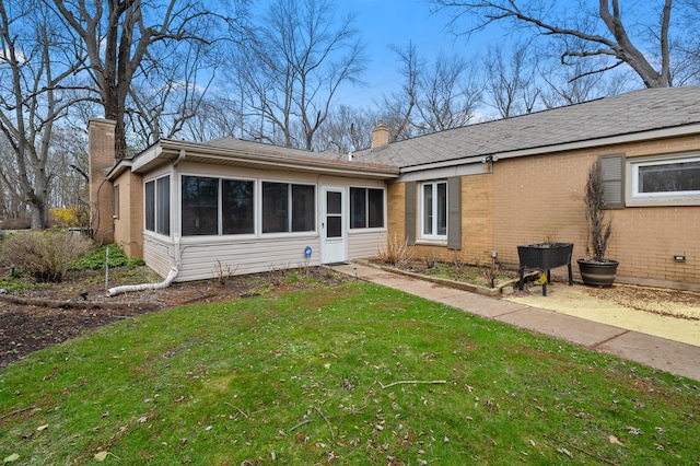 rear view of property featuring brick siding, a sunroom, a lawn, and a chimney
