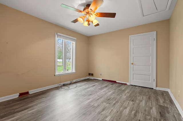 unfurnished room with visible vents, baseboards, a ceiling fan, attic access, and wood finished floors