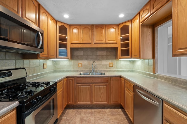 kitchen featuring appliances with stainless steel finishes, decorative backsplash, a sink, and glass insert cabinets
