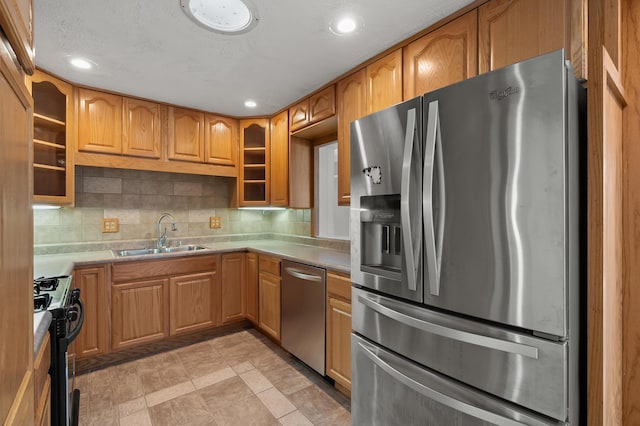 kitchen featuring tasteful backsplash, glass insert cabinets, a sink, light countertops, and stainless steel appliances