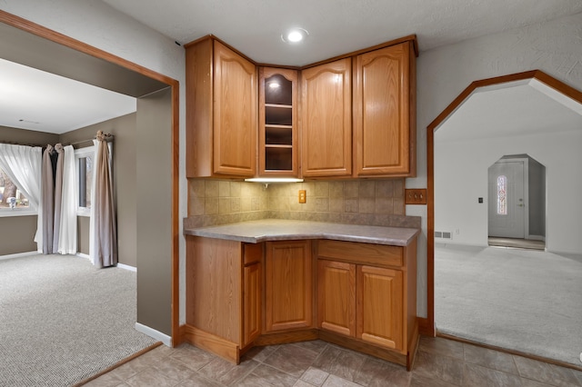 kitchen featuring light carpet, decorative backsplash, light countertops, and glass insert cabinets