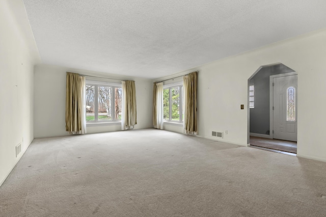 carpeted spare room with arched walkways, visible vents, and a textured ceiling