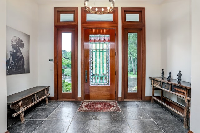 entrance foyer with a chandelier, stone tile flooring, and baseboards