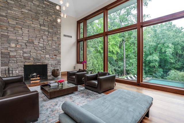 living area featuring wood finished floors, a stone fireplace, plenty of natural light, and a towering ceiling