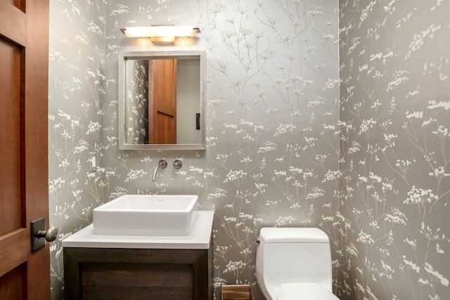 half bathroom featuring wallpapered walls, toilet, and vanity