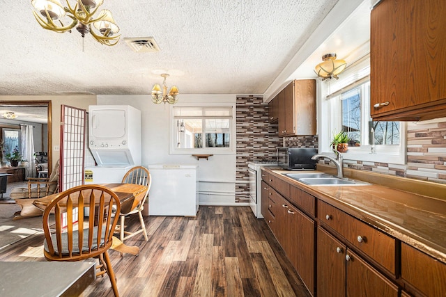 kitchen featuring visible vents, a chandelier, gas range gas stove, stacked washer and dryer, and fridge