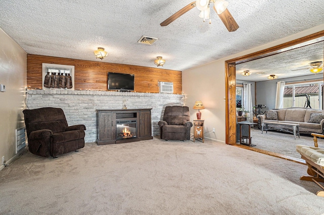 carpeted living area with a textured ceiling, ceiling fan, a fireplace, and visible vents