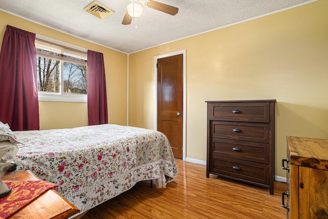 bedroom featuring baseboards, a textured ceiling, visible vents, ceiling fan, and light wood finished floors