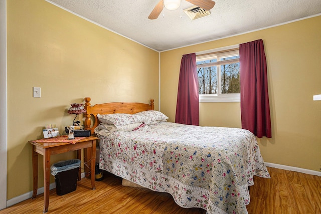 bedroom featuring visible vents, baseboards, wood finished floors, and a textured ceiling